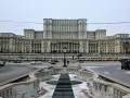 Imponujący budynek parlamentu w Bukareszcie, z monumentalną fasadą i otaczającym go placem z fontanną.