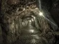 Wąski korytarz oświetlony lampami, prowadzący w głąb ziemi. Kamienne ściany i wilgotna posadzka tworzą atmosferę tajemniczych sztolni walimskich.