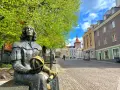 Pomnik Kopernika na olsztyn rynek, z kolorowymi kamienicami w tle i zielonymi drzewami.