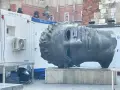 Monumentalna głowa na rynku w Krakowie, z pustymi oczodołami, stoi obok białych kontenerów.