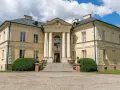 Elegancki pałac w Dobrzycy z kolumnowym portykiem i żółtą fasadą, otoczony zielenią.