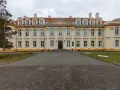 Pałac biskupów kujawskich w Wolborzu, okazała budowla z żółtą fasadą i czerwonym dachem, otoczona zielenią i brukowanym podjazdem.