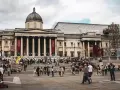 Tłum ludzi przed National Gallery w Londynie. Monumentalna fasada z kolumnami i kopułą, czerwone banery zapraszają do zwiedzania.