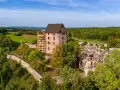 Zamek Świny, częściowo odrestaurowany, góruje nad zielonym krajobrazem. Ruiny zamku i otaczający las tworzą malowniczą scenerię.