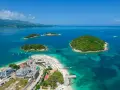 Albania Durrës atrakcje: malownicze wysepki z zieloną roślinnością otoczone turkusową wodą, plaża z leżakami i budynkami hotelowymi.