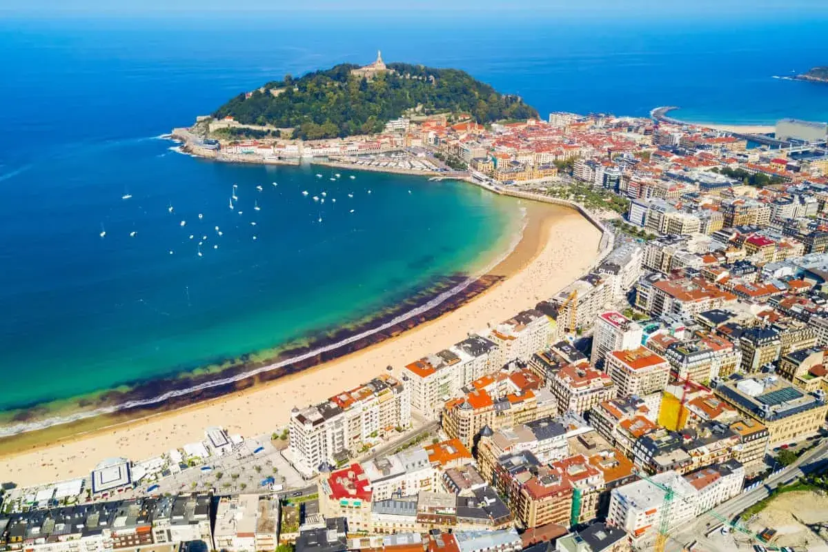 Widok z lotu ptaka na zatokę La Concha w San Sebastian, z piaszczystą plażą, turkusową wodą i zabudową miejską.