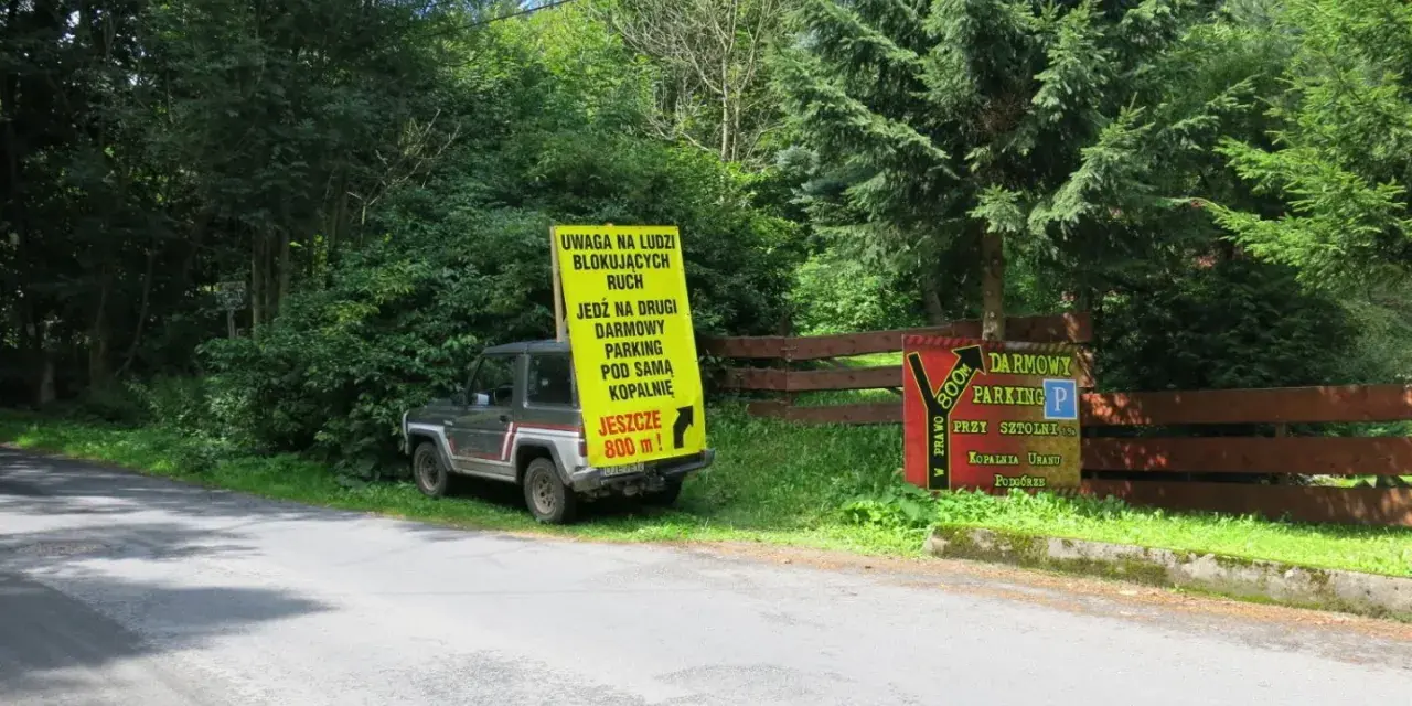 Samochód terenowy przy drodze, obok żółty znak informujący o darmowym parkingu przy sztolni kowary.