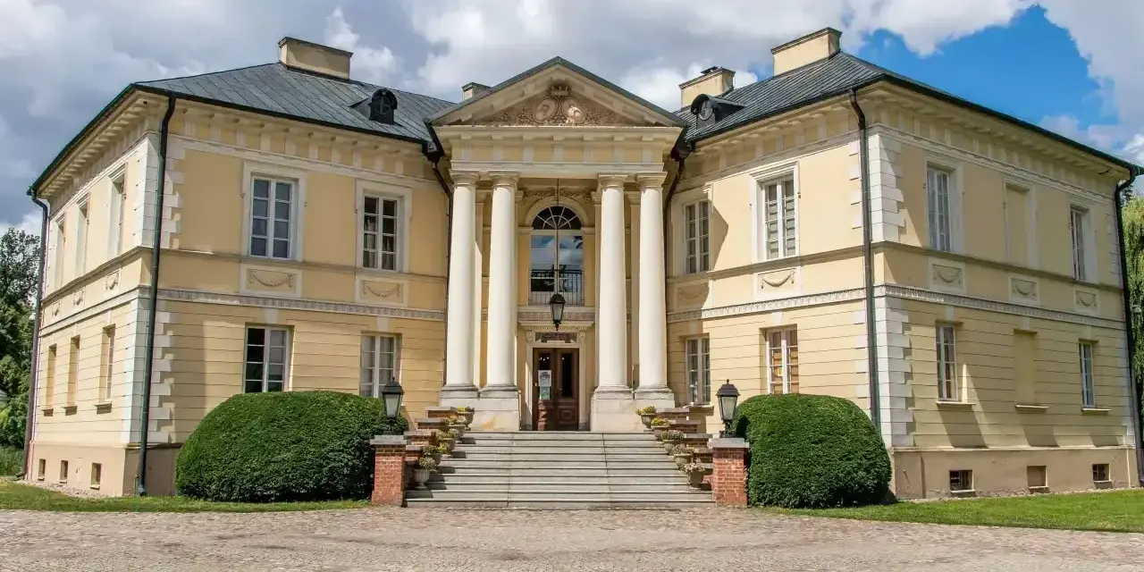 Elegancki pałac w Dobrzycy z kolumnowym portykiem i żółtą fasadą, otoczony zielenią.