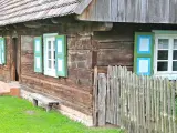 Drewniana chata z zielono-niebieskimi okiennicami, ławką i płotem. Skansen w Dziekanowicach zaprasza do podróży w czasie.