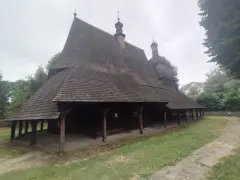 Drewniany kościół w Sękowej z charakterystycznym, wielospadowym dachem krytym gontem, otoczony zielenią.