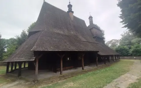 Drewniany kościół w Sękowej z charakterystycznym, wielospadowym dachem krytym gontem, otoczony zielenią.