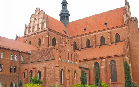 Potężny zamek krzyżacki w Pelplinie, z cegły i czerwonym dachem, góruje nad okolicą.
