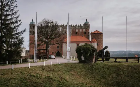 Zamek Golub-Dobrzyń zaprasza na zwiedzanie. Potężna twierdza z armatą na dziedzińcu, otoczona zielenią i drzewami.