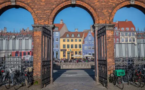 Kolorowe kamienice nad kanałem, idealne na szybkie zwiedzanie Kopenhagi w jeden dzień. Rowerzyści czekają na przejazd.