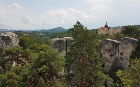 Widok na zamek Hrubá Skála otoczony skalnymi formacjami i lasem.