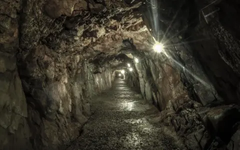 Wąski korytarz oświetlony lampami, prowadzący w głąb ziemi. Kamienne ściany i wilgotna posadzka tworzą atmosferę tajemniczych sztolni walimskich.