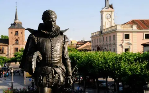 Pomnik Cervantesa w Alcalá de Henares, z ratuszem i wieżą zegarową w tle.