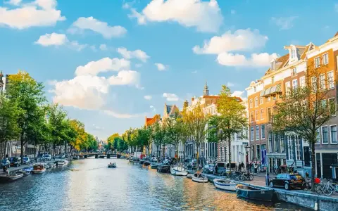 Widok na kanał w Amsterdamie, z łodziami, kamienicami i zielenią. Idealne miejsce na spacer, gdzie jest Amsterdam.