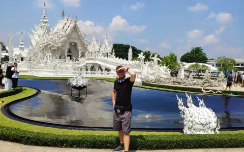 Mężczyzna pozuje przed olśniewającą białą świątynią Wat Rong Khun w Chiang Rai.