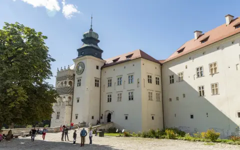 Zamek w Pieskowej Skale z charakterystyczną wieżą zegarową i renesansową attyką. Zwiedzający spacerują po dziedzińcu.
