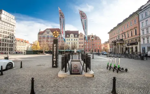Wejście do podziemi z napisem "Movie Gate Wrocław" na placu w otoczeniu zabytkowych kamienic.