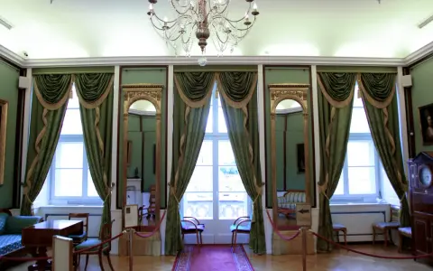 Wnętrze pałacu królewskiego we Wrocławiu. Eleganckie zielone zasłony, złote lustra i kryształowy żyrandol tworzą atmosferę dawnej świetności.