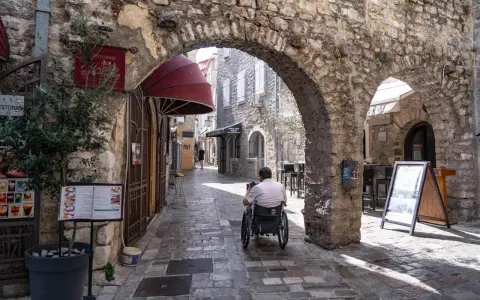 Mężczyzna na wózku inwalidzkim przemierza urokliwe, kamienne uliczki **Budva stare miasto**.