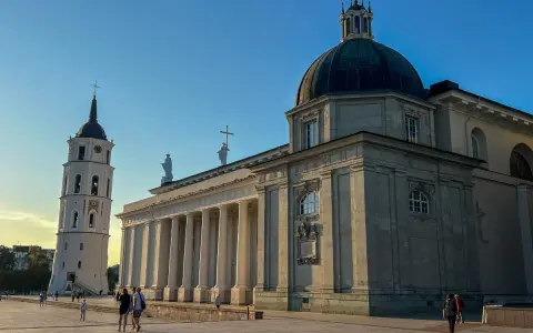 Wileńskie kościoły: Katedra i dzwonnica na placu. Słońce oświetla monumentalną architekturę, tworząc długie cienie.
