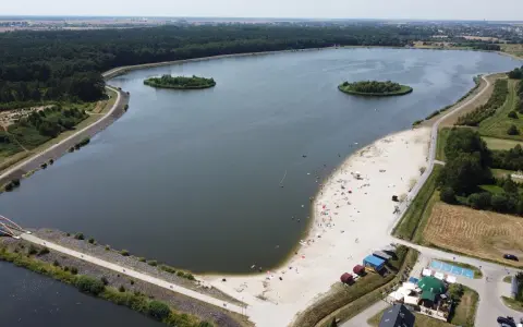 Opolskie atrakcje: piaszczysta plaża nad jeziorem, wyspy, las i mostek. Ludzie odpoczywają i kąpią się.
