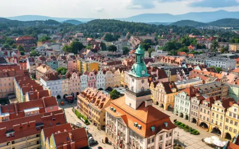 Widok z lotu ptaka na kolorowy rynek starego miasta z wieżą ratuszową i górzystym tłem.