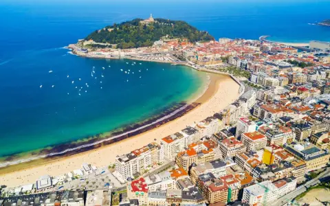 Widok z lotu ptaka na zatokę La Concha w San Sebastian, z piaszczystą plażą, turkusową wodą i zabudową miejską.
