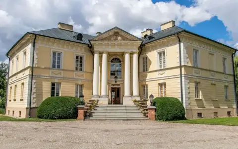 Elegancki pałac w Dobrzycy z kolumnowym portykiem i żółtą fasadą, otoczony zielenią.