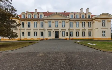 Pałac biskupów kujawskich w Wolborzu, okazała budowla z żółtą fasadą i czerwonym dachem, otoczona zielenią i brukowanym podjazdem.