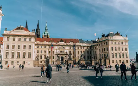 Tłum turystów spaceruje po dziedzińcu przed imponującym zamkiem na Hradczanach.