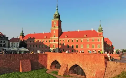 Słoneczny dzień na placu zamkowym w Warszawie. Ludzie odpoczywają na murze przy Zamku Królewskim.