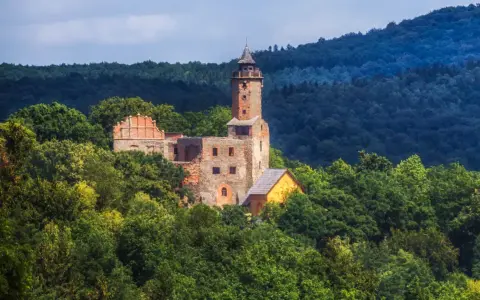 Ruiny zamku w **Zagórzu Śląskim** w otoczeniu bujnej zieleni. Wieża i fragmenty murów wznoszą się pośród drzew.