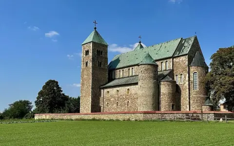 Kamienny zamek w Tumie z zielonym dachem, otoczony murem i zieloną łąką, pod błękitnym niebem.
