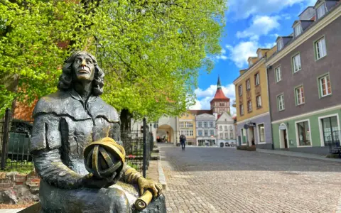 Pomnik Kopernika w Olsztynie, na tle kolorowych kamienic i błękitnego nieba. Jura Krakowsko-Częstochowska wita wiosną.