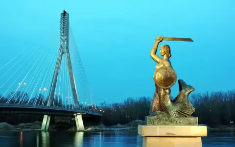 Syrenka warszawska z mieczem i tarczą stoi nad Wisłą, w tle nowoczesny most.