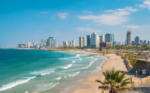 Słoneczna tel aviv plaża z turkusową wodą i nowoczesnymi wieżowcami w tle.
