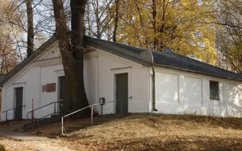 Ohel cadyka Elimelecha w Leżajsku zwiedzanie. Biały budynek z drzwiami i oknem, otoczony drzewami jesienią.