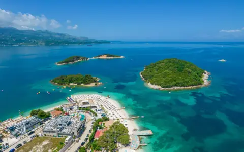 Albania Durrës atrakcje: malownicze wysepki z zieloną roślinnością otoczone turkusową wodą, plaża z leżakami i budynkami hotelowymi.