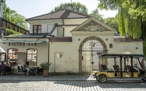 Bistro Bar obok bramy z hebrajskimi napisami, charakterystycznej dla krakowskiej dzielnicy żydowskiej. Obok stoi żółty meleks.
