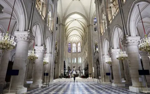 Wnętrze katedry Notre Dame, z monumentalnymi kolumnami, sklepieniem i witrażami. Na środku nawy stoi samotna postać.