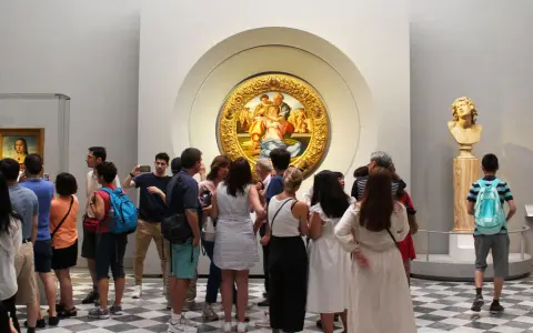 Galeria Uffizi: co zobaczyć? Grupa turystów podziwia okrągły obraz w złotej ramie i rzeźbę.