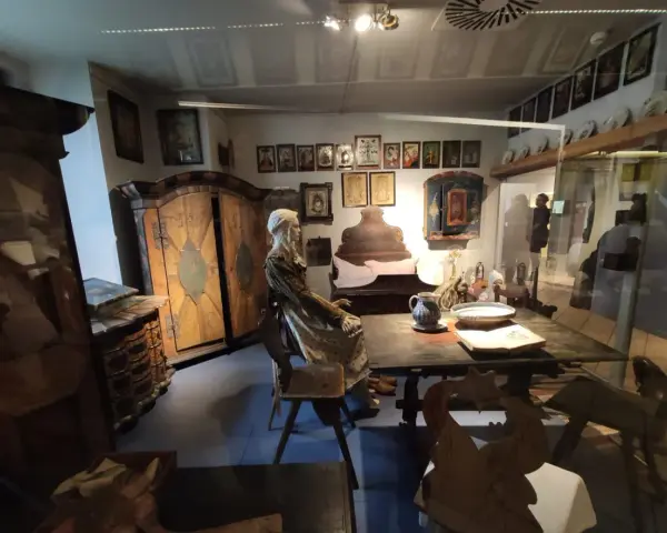 Wrocław Muzeum Etnograficzne: ekspozycja dawnej izby z manekinem w stroju ludowym, zdobionymi meblami i obrazami na ścianach.