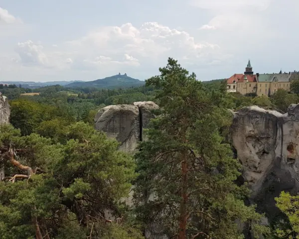 Widok na zamek Hrubá Skála otoczony skalnymi formacjami i lasem.