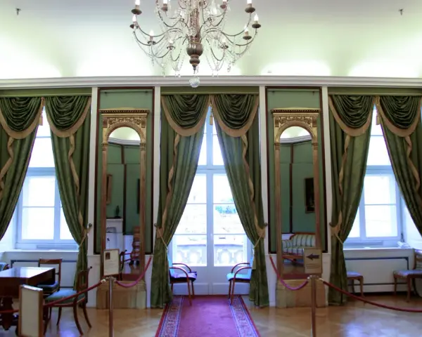 Wnętrze pałacu królewskiego we Wrocławiu. Eleganckie zielone zasłony, złote lustra i kryształowy żyrandol tworzą atmosferę dawnej świetności.