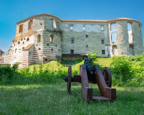 Zamek w Janowcu, ruiny warowni z armatą na pierwszym planie, pod błękitnym niebem.