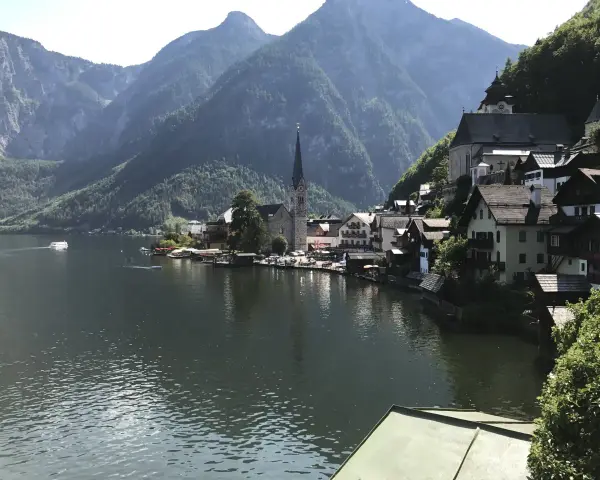 Malowniczy widok na Hallstatt, miasteczko nad jeziorem, z górami w tle. Widać kościół i domy, a na wodzie statek. To miejsce słynie z kopalni soli.